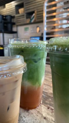 three drinks sitting on top of a table next to each other in plastic cups with lids