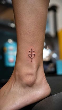 a small cross and heart tattoo on the side of someone's foot by person