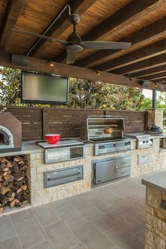 an outdoor kitchen with grills and television on the wall