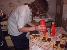 a woman is making pizzas in the kitchen with an orange bottle and saucer