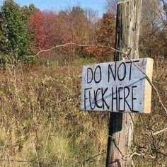 a sign that says do not flush here on a wooden pole in the middle of a field