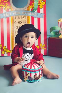 a baby sitting on the floor in front of a circus tent and holding a cupcake