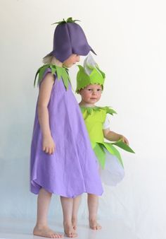 two children dressed in costumes standing next to each other on a white surface with one child wearing a green and purple costume