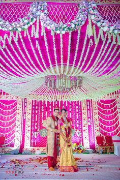 a couple posing for a photo in front of a stage decorated with flowers and garlands