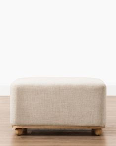 an upholstered footstool on a wooden floor in front of a white wall