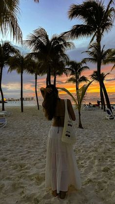 a woman standing on top of a sandy beach next to palm trees and the ocean