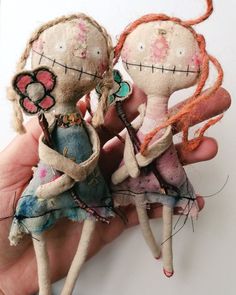 two handmade dolls sitting next to each other on a white surface in front of a person's hand