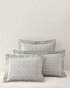 three pillows on a bed with white sheets and blue flowered pillow cases in the background