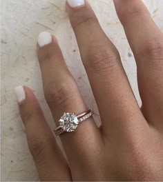 a woman's hand with a diamond ring on top of her finger and white nail polish