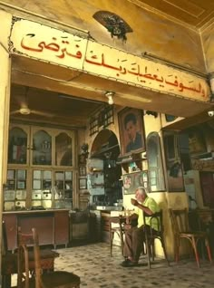 an old man sitting at a table in front of a building with arabic writing on it