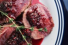 some meat with cranberry sauce on a white and blue plate topped with green sprigs