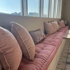 a long couch with many pillows on top of it next to a table and windows