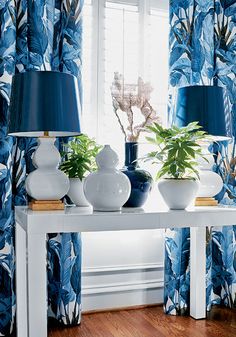 a white table topped with two lamps next to a window covered in blue and white curtains