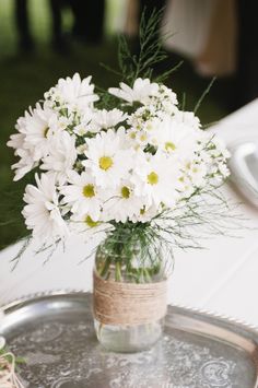 a vase filled with white flowers sitting on top of a metal tray next to a table