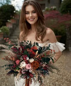 a woman in a white dress holding a bouquet of flowers and foliage on her wedding day