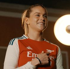 a woman in an orange and white shirt smiles at the camera with a light behind her