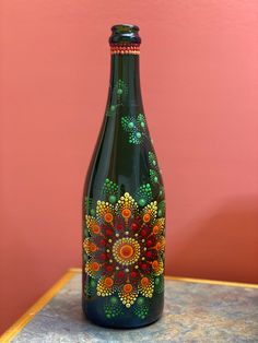 a green bottle with colorful designs painted on it sitting on top of a table next to a pink wall