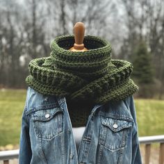 a woman wearing a denim jacket with a green scarf around her neck and a wooden hanger in front of her