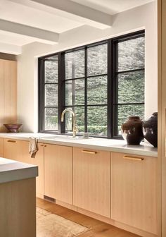 a kitchen with wooden cabinets and white counter tops next to a large window that has black panes on it