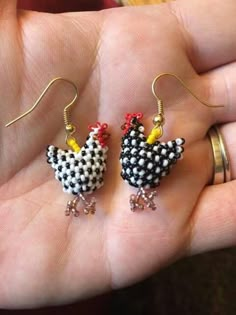 a person is holding two small chicken earrings