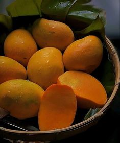 a basket filled with lots of oranges on top of a wooden table next to green leaves