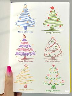 a hand holding an open book with christmas tree drawings on the front and back cover