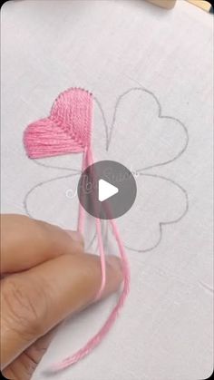 someone is stitching a heart on a piece of paper with pink thread and yarn