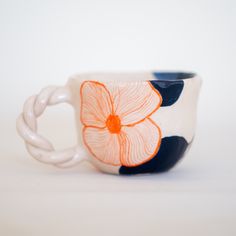 a coffee cup with an orange flower painted on the side and black rim, sitting on a white surface