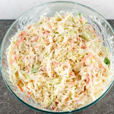 a glass bowl filled with coleslaw and carrots next to a wooden spoon