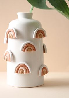 a white vase with rainbows on it and a green plant in the back ground