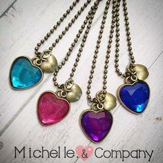 four heart shaped necklaces hanging from chains on a white wooden surface with the words michael lee & company written below them