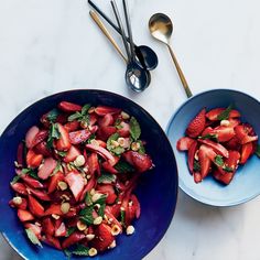 two blue bowls filled with strawberries and other fruit salads next to each other