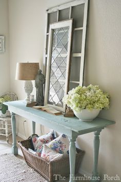 a blue table with a mirror and flowers on it in front of a white wall