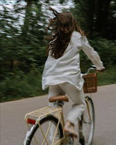 a woman riding a bike down a street with trees in the backgrouds