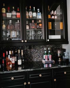 a black cabinet with liquor bottles and glasses on it's glass doors, next to a granite counter top