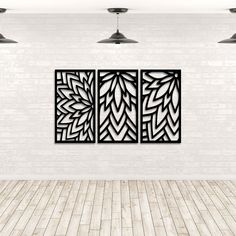 three black metal wall art pieces on a white brick wall in an empty room with wood flooring