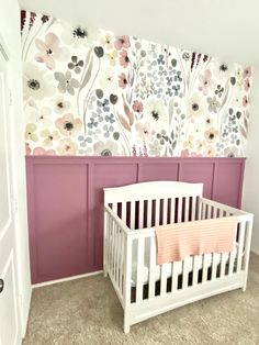 a white crib in front of a wall with flowers painted on it and a pink blanket draped over the crib