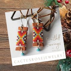 a pair of earrings with colorful beads hanging from it's earwires next to pine cones