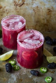 two red drinks with limes and blackberries on the side