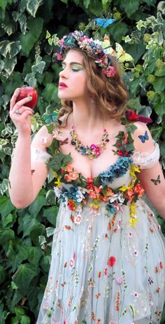 a woman in a dress with flowers and butterflies on her chest, holding an apple