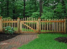 a wooden gate in the middle of a brick walkway surrounded by green grass and trees