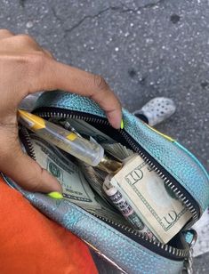 a person holding a purse full of money and plastic pens in their left hand, with one dollar bill sticking out of it