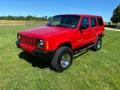 a red jeep parked on top of a lush green field