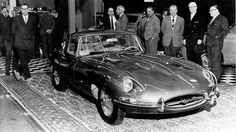 a group of men standing around a black and white car