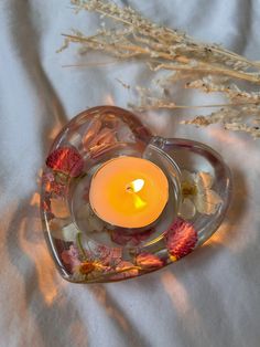 a heart shaped glass candle holder with flowers in the center on a white cloth background