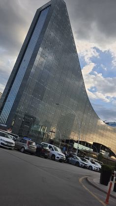 cars are parked in front of a tall building with a triangular design on it's side