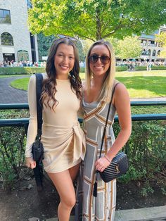 two women standing next to each other in front of a fence and grass covered park