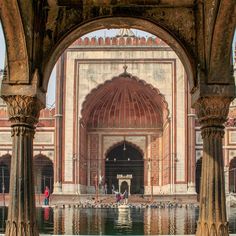 the entrance to an old building with pillars and arches in front of it, surrounded by water