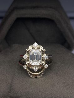 a fancy ring with an emerald center surrounded by smaller round brilliant cut diamonds in a velvet box