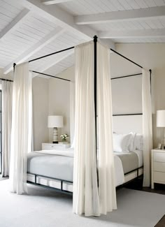 a bedroom with four poster bed and white curtains